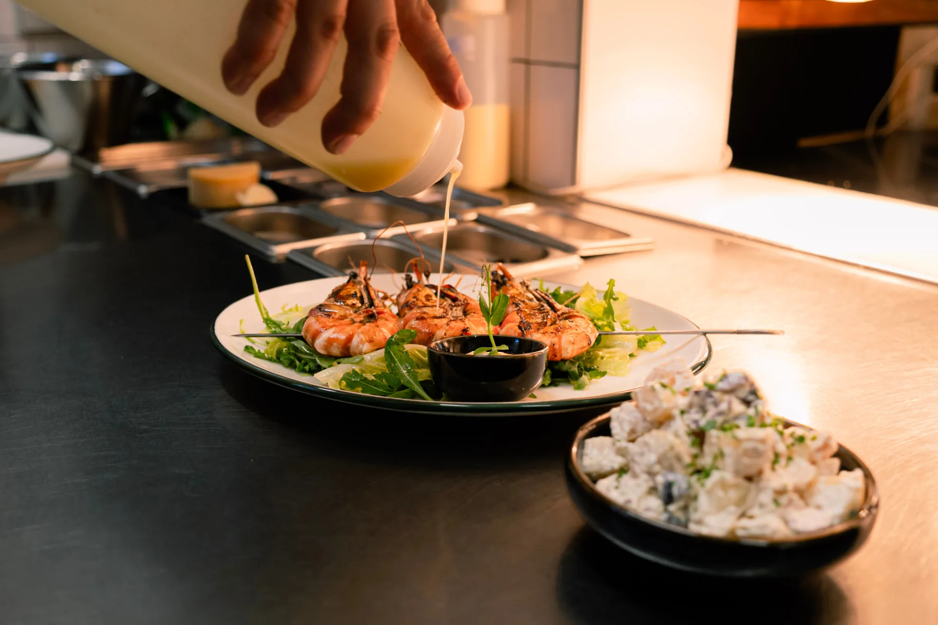 Kok hos CAVU krydrer grillede rejer med dressing på anrettet tallerken i køkkenet